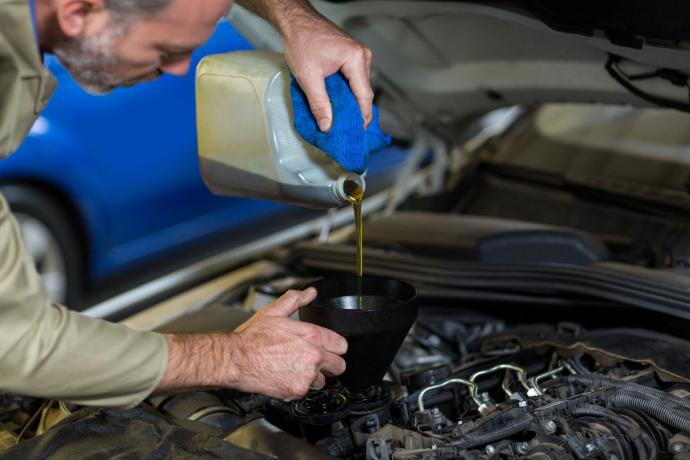 Aceite de motor; un hombre con barba echando en un embudo un líquido para el auto 